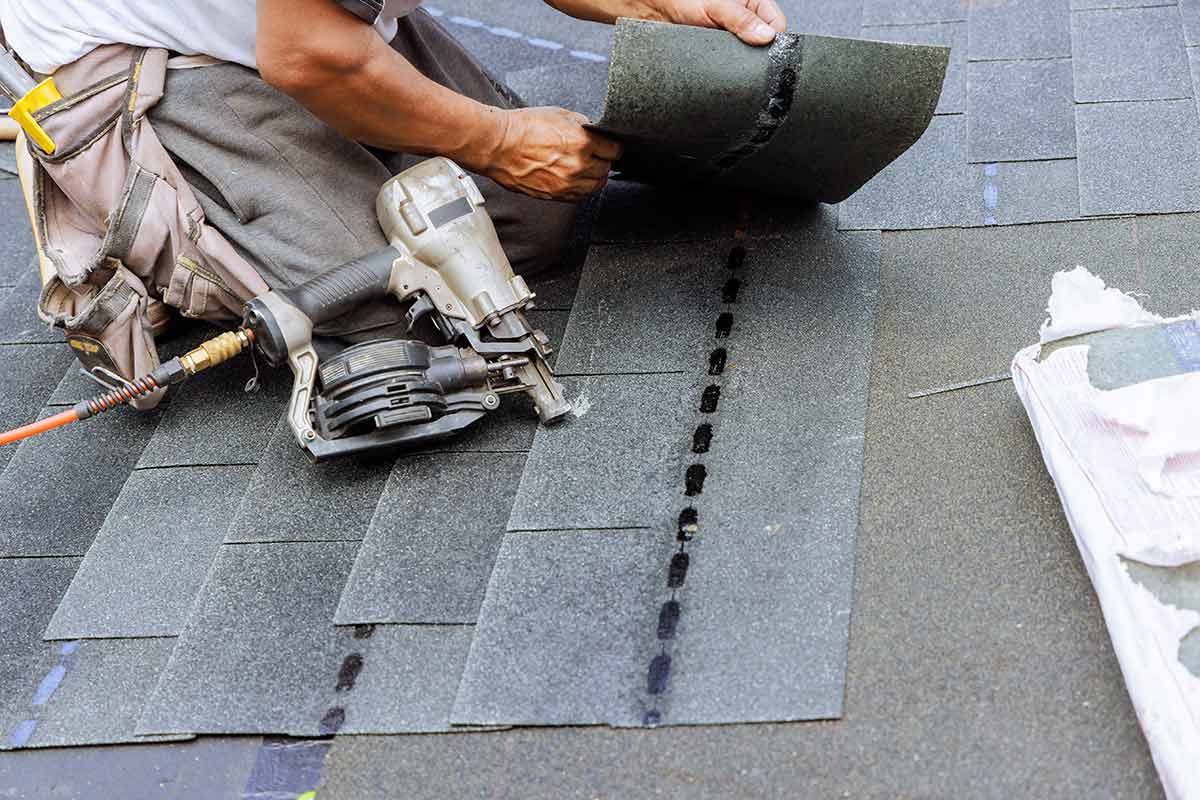 A roofer using a nail gun to install shingles